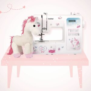 Nähmaschine mit Einhorn Sticker Design und Einhorn Kuscheltier als Deko steht auf einem rosa Tisch